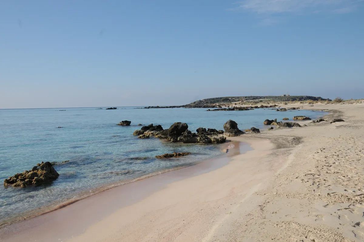 Pink-tinged sand and shallow water at the waterline of Elafonisi beach, Crete